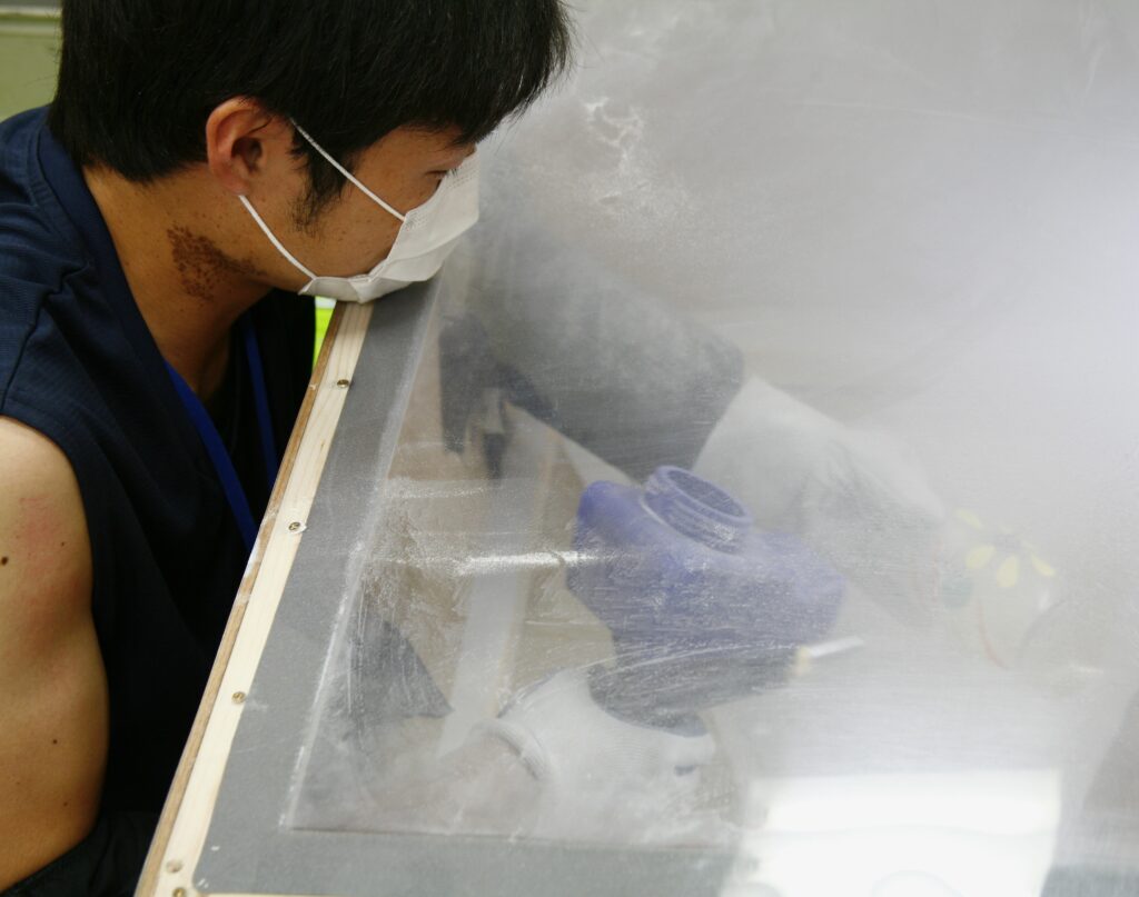 サンドブラスト作業の様子　箱の中で砂を吹き付けています